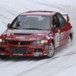En röd rallybil kör nerför en snöig backe. (AI text)