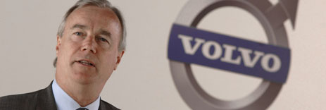 En man i kostym står framför Volvos logotyp. (AI text)