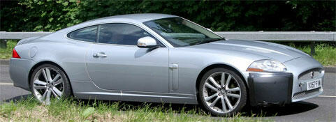En silverfärgad Jaguar XKR sportbil kör nedför en landsväg. (AI text)
