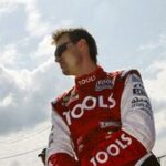 En racerbilförare står bredvid en bil. (AI text)