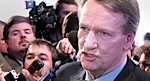 En man i kostym och slips omges av reportrar. (AI text)