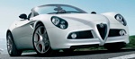 En vit Alfa Romeo sportbil kör nedför en väg. (AI text)