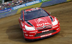 En röd Citroën C3 rallybil kör på en grusväg. (AI text)