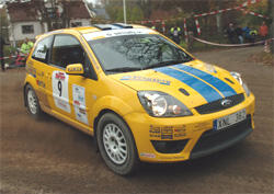 En gul Ford Fiesta rallybil kör nedför en grusväg. (AI text)