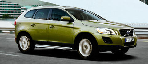 En grönt Volvo XC90 SUV kör ner en stadsgata. (AI text)