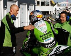 En grön motorcykel med en man på den och en man stående bredvid. (AI text)