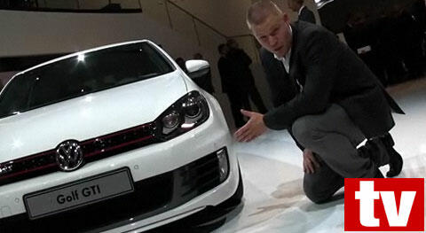 En man knäböjer bredvid en vit Volkswagen Golf GTI. (AI text)