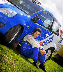 En man i blå kostym sitter på gräset bredvid en blå bil. (AI text)