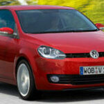 En röd Volkswagen Polo kör nerför en väg. (AI text)