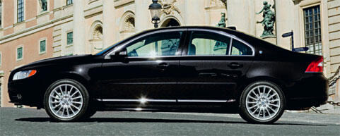 En svart Volvo S60 parkerad framför ett byggnad. (AI text)