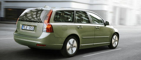 En grönt Volvo V60 stationwagon kör nedför en stadsgata. (AI text)