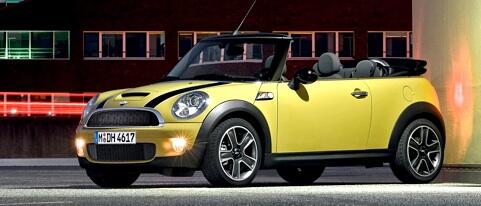 En gul Mini Cooper cabriolet parkerad framför ett byggnad. (AI text)