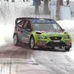 En rallybil kör nerför en snöig väg. (AI text)