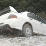 En vit bil kör nerför en snöig backe. (AI text)