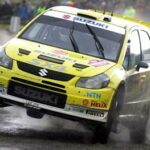 En rallybil kör genom en blöt och smutsvåt yta. (AI text)