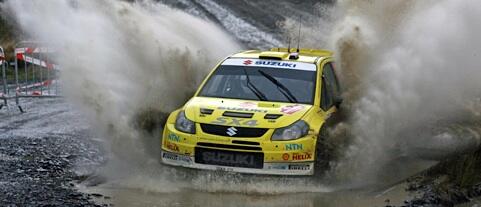 En gul Suzuki Rally-bil kör genom en smutsig yta. (AI text)