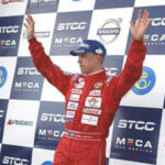 En racerförare i en röd racerdräkt står på pallen. (AI text)