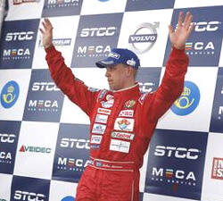 En racerförare i en röd racerdräkt står på pallen. (AI text)