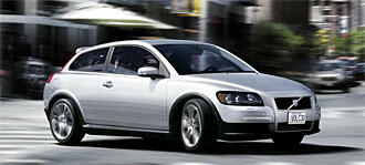 En vit bil körer nerför en stadsgata. (AI text)