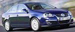En blå Volkswagen Jetta kör nerför vägen. (AI text)