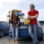 En par personer står bredvid en blå bil. (AI text)