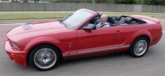 En röd Ford Mustang cabriolet kör nerför en väg. (AI text)