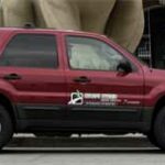 En röd Ford Escape står parkerad framför ett byggnad. (AI text)