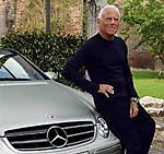 En man står lutad mot en silverfärgad Mercedes-Benz SLK. (AI text)