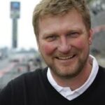 En man leende framför en racerbana. (AI text)