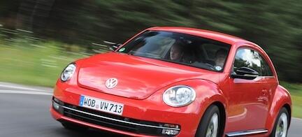 En röd Volkswagen Käfer kör nerför en väg. (AI text)