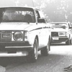 En man sitter vid vägkanterna med en bil i bakgrunden. (AI text)