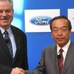 Två män skakar hand inför en Toyota. (AI text)