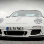 En vit Porsche 911 GTS kör nerför en väg. (AI text)