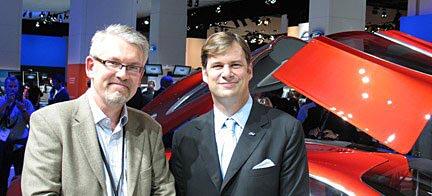 Två män står bredvid en röd bil. (AI text)