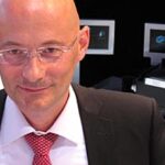 En man i kostym och slips sitter i en bil. (AI text)