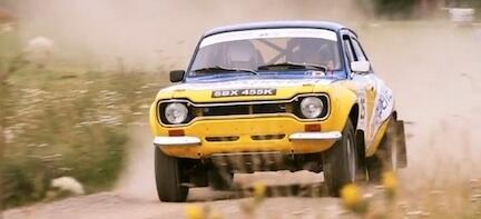 En gul och vit rallybil kör nerför en grusväg. (AI text)