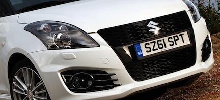 En vit Suzuki Swift parkerad vid en grusväg. (AI text)