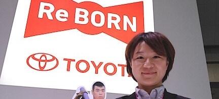 En kvinna i kostym håller en återskapat Toyota-bil. (AI text)