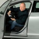 En man står parkerad framför en bil och laddar den. (AI text)