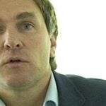 En man i kostym pratar inför en kamera. (AI text)