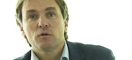 En man i kostym pratar inför en kamera. (AI text)