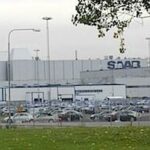 En bil står parkerad framför en fabrik. (AI text)