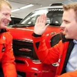 Två män i röda jackor står bredvid en röd Mini. (AI text)