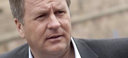 En man i kostym och slips tittar på kameran. (AI text)