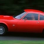 En röd sportbil kör nerför en väg. (AI text)