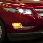 En röd Chevrolet Volt kör nerför en stadsgata. (AI text)