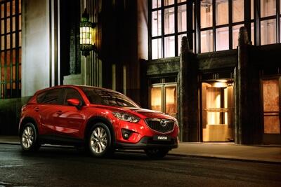 En röd Mazda CX-5 parkerad framför ett byggnad. (AI text)