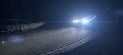 En bil kör nerför en bergsväg på natten. (AI text)