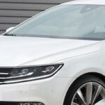 En vit Volkswagen Passat parkerad framför en garageport. (AI text)