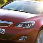 En röd Opel Astra kör nerför en landsväg. (AI text)